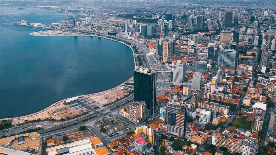 An aerial view of a Angola city with tall buildings in the center, Luanda, Angola. The city is situated on the coast, next to a large body of water, likely the Atlantic Ocean.