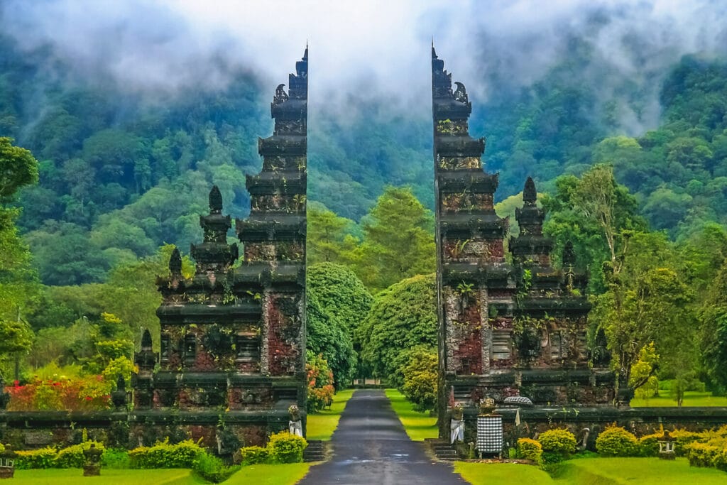 The image is of Bali Indionesia top travel place to visit. An image of a picturesque Balinese temple standing tall amidst the towering trees of a vibrant forest.