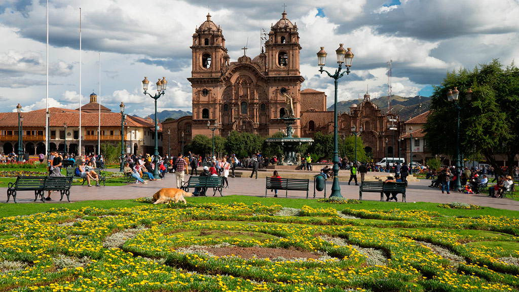 A scenic view of Plaza Mayor de Cusco, a central square in Cusco, Peru. The image features Catedral del Cusco, a Cusco landmark, and other buildings surrounding the square.