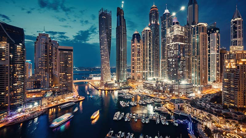 A night view of a harbor with boats at Dubia UAE. There are skyscrapers in the background.