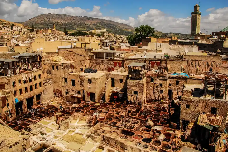 An aerial view of a Fez Morocco with many buildings close together. In the distance is a large, white building with a dome and four minarets. This building is likely a mosque.