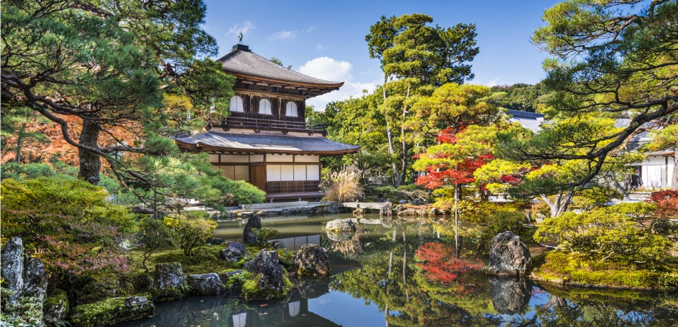 This photo is of Kyoto Japan a top place to travel, A photo of the Kinkaku-ji, a golden pavilion temple, reflected in a pond in Kyoto, Japan. The temple is surrounded by trees with green leaves.