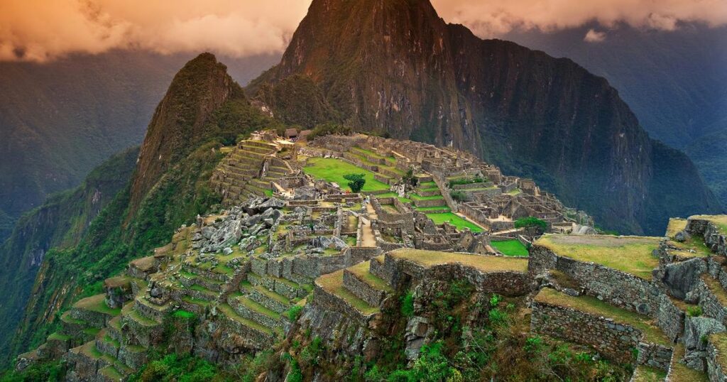 The image shows the Machu Picchu, Peru The top place to travel. In this image there is mountains and lush green grass.