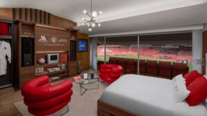 The image shows the The Manchester United-themed suite in Dubai. In this image there is bed and sofa on the front the football ground is there