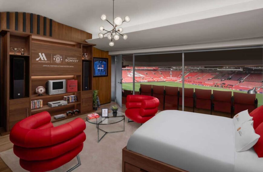 The image shows the The Manchester United-themed suite in Dubai. In this image there is bed and sofa on the front the football ground is there