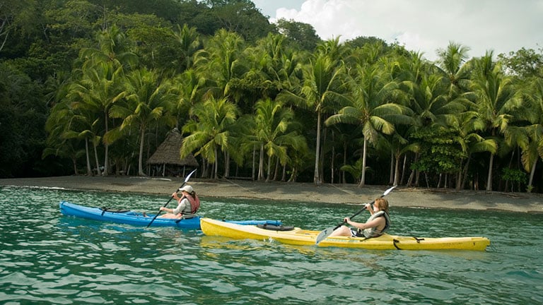 This imgae is of  Osa Peninsula, Costa Rica
there is a lake where two peoples are on boats. in the back there are trees and a beautiful view. 