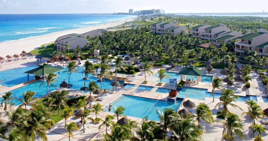 This image is of Tulum Mexico a top travel place to visit. This image is a bird's-eye view of a tropical resort complex with sparkling blue pools, lounge chairs, and swaying palm trees.