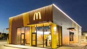 The picture is of the mcdonalds resturant decorated for the 4th july. There is logo of the MCD in the front and here the topis is Is McDonald’s Open On July 4th 2024?