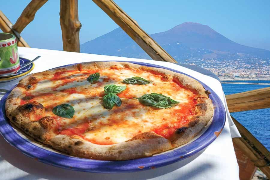 Image is of pizza at naples itlay and behind is the beautiful view of the nature wow the best destination for the food lovers