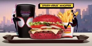 A red Whopper burger with a sesame seed bun on a black tray, next to a cup with a Spider-Man logo and a container of French fries. Spider-Man is swinging down from the top of the image and Gwen Stacy is climbing the side of the cup.