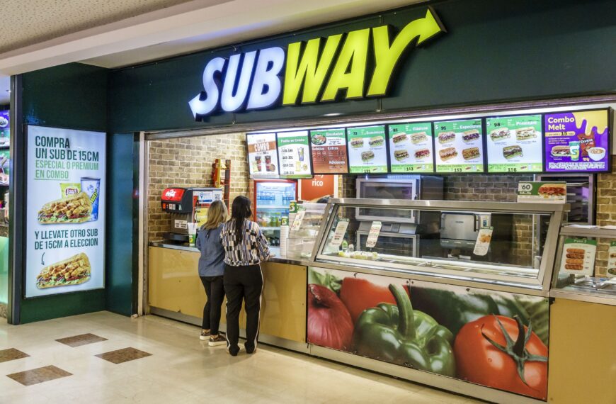 The picture shows the subway restaurant and some of ladys looking for the subway menu with prices.