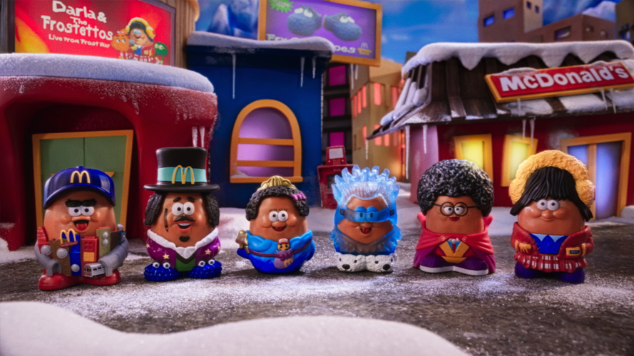 Five small potato-shaped toys are standing in a row. They are wearing different costumes, including a magician's hat, a superhero cape, and a winter hat. The background shows a snowy cityscape with a McDonald's restaurant.