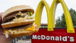 A person's hand holding a Big Mac with a McDonald's restaurant in the background. The Big Mac is dripping with special sauce and melted cheese. Is this a clue to the McDonald's Secret Menu?