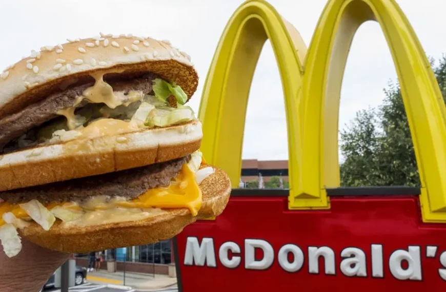 A person's hand holding a Big Mac with a McDonald's restaurant in the background. The Big Mac is dripping with special sauce and melted cheese. Is this a clue to the McDonald's Secret Menu?