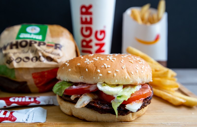 A delicious Burger King Whopper, served with a side of crispy fries and a refreshing beverage. The burger features a sesame seed bun, a flame-grilled beef patty, lettuce, tomato, onion, pickles, and ketchup.