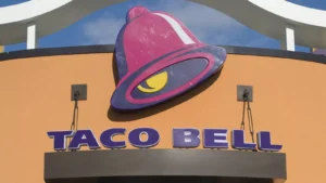 A Taco Bell restaurant sign featuring the signature purple and pink bell logo, with the words "Taco Bell" displayed below. Take advantage of Taco Bell Deals Box for exclusive offers!