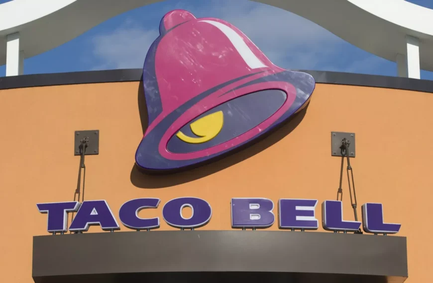 A Taco Bell restaurant sign featuring the signature purple and pink bell logo, with the words "Taco Bell" displayed below. Take advantage of Taco Bell Deals Box for exclusive offers!