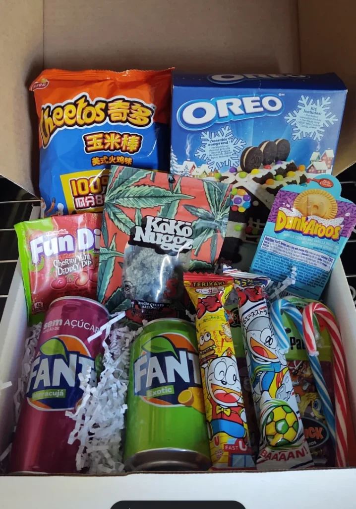 A gift box filled with various snacks and candies from around the world. Some of the items visible include Cheetos, Oreos, Fun Dip, Froot Loops, Fanta soda, and a Doraemon candy. The box also contains some snacks with unfamiliar packaging and labeling. The Best food gifts for christmas 