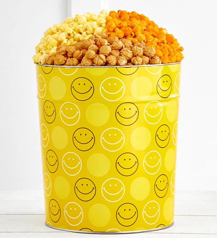 A large tin filled with popcorn. The tin is yellow with a smiley face pattern. The popcorn is a mix of caramel and cheddar flavors.