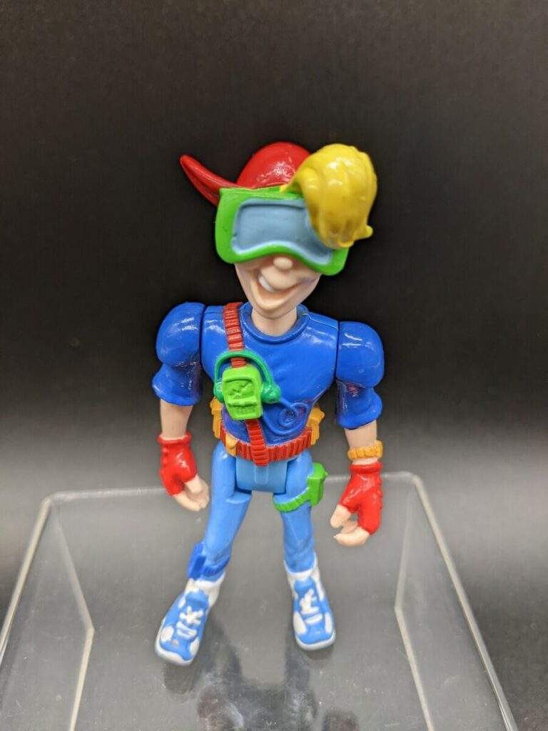 A vintage action figure of Kid Vid, a character from the 1990s animated series "Kid Vid." The figure is wearing a red hat, green goggles, a blue jersey, and red gloves. He has a yellow hairpiece and is holding a green Walkman-style device.