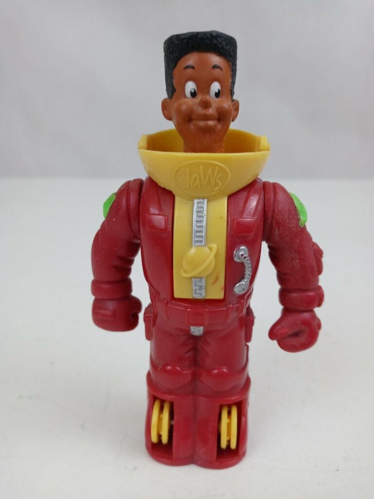 A vintage action figure of a young boy dressed as an astronaut. The figure has a brown head, a red spacesuit with a yellow stripe, and green accents. He is wearing roller skates and has a phone on his chest. The "Jaws" logo is visible on his suit.