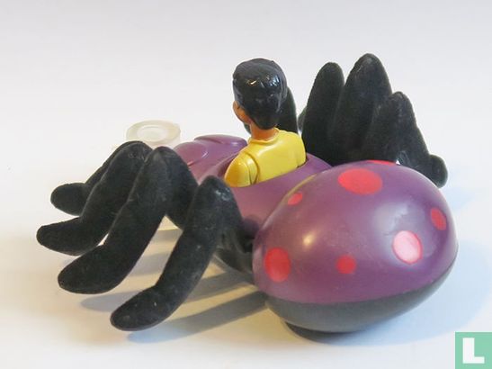  A Burger King Bug Riders lingo toy featuring a man driving a large, purple spider. The spider has eight long legs and red dots on its body. The man is wearing a yellow shirt and is holding a steering wheel.